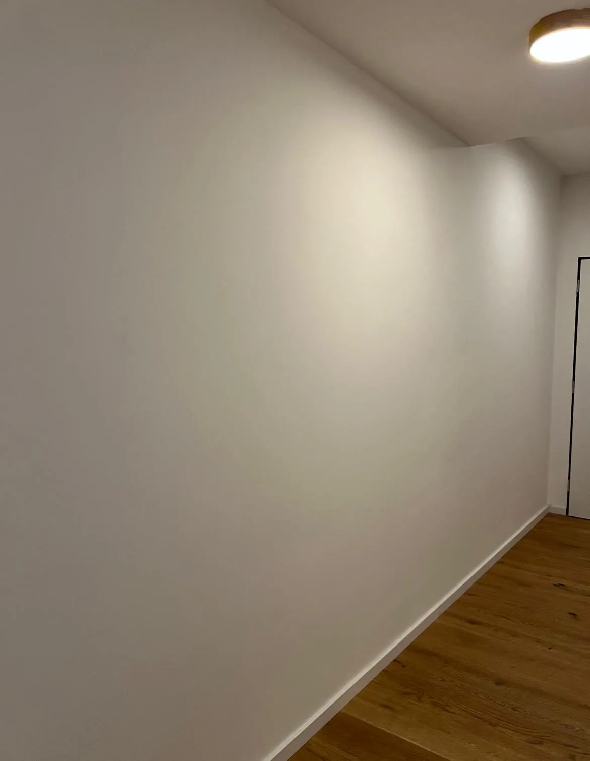 Hotová hladká bílá stěna chodby po dokončeném nátěru.