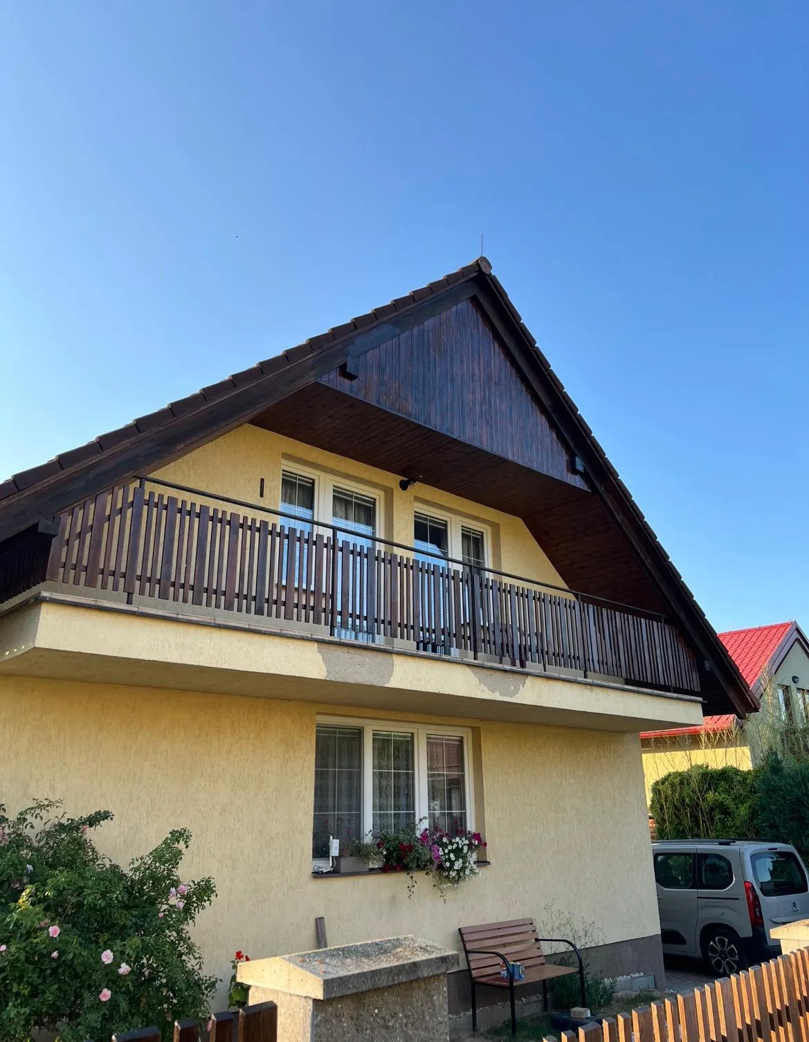 Rodinný dům se žlutou fasádou a tmavým dřevěným štítem a balkonem.
