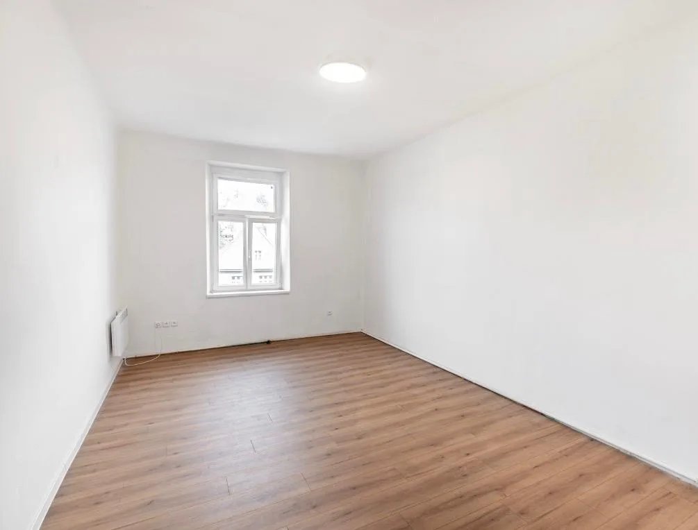 Světlý pokoj po vymalování do bílé s dřevěnou plovoucí podlahou.