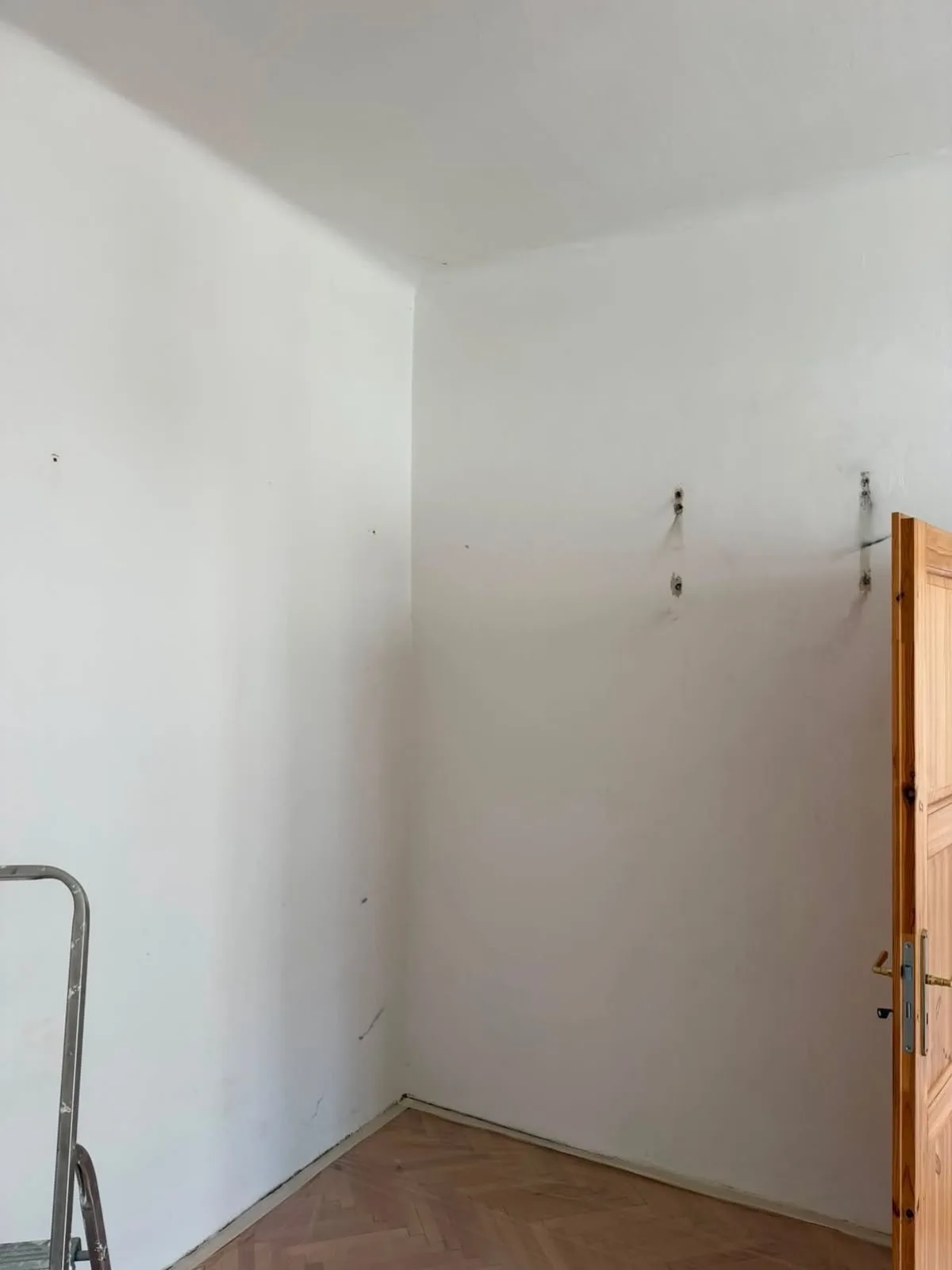 Rozpracovaná malba bílých stěn v prázdném pokoji s parketami.