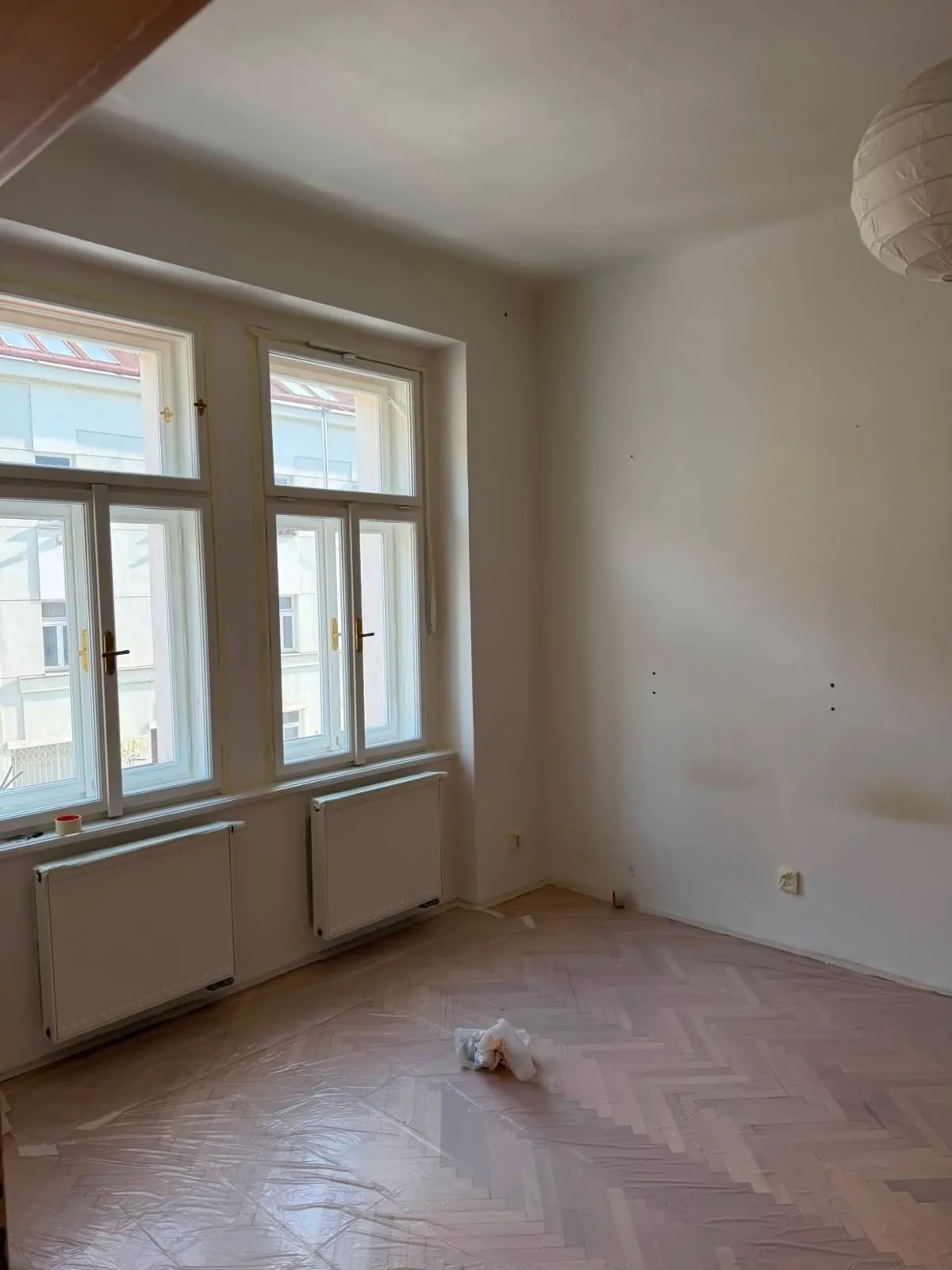 Pokoj se dvěma okny během malování, podlaha zakrytá ochrannou fólií.