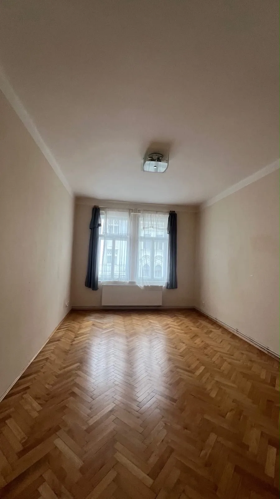 Prázdný pokoj s parketami a oknem před rekonstrukcí nátěru.