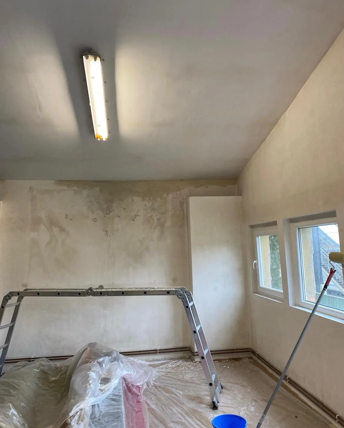 Pokoj během malování se zakrytou podlahou a žebříkem.